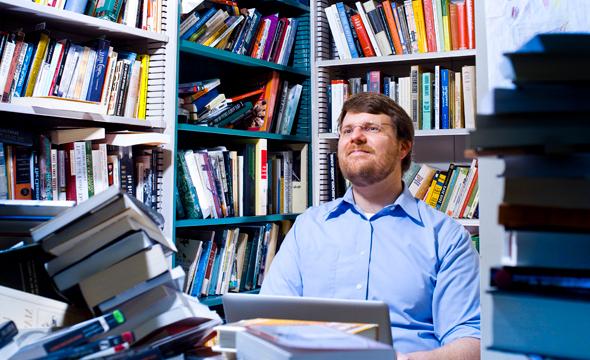 A white man with a goatee looking up in an office covered with bookshelves