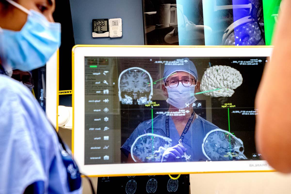 爱德华·张(爱德华常)在手术中在屏幕上的倒影中，屏幕上有多个大脑图