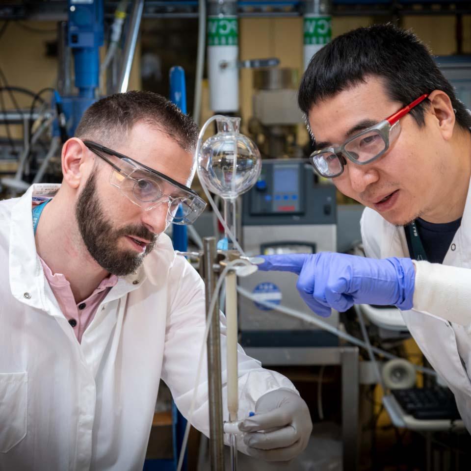 两个学生化学家戴着护目镜、手套和实验服进行实验