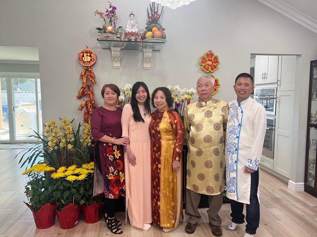 Chelsey阮, 与家人合照, 包括她的祖父, 穿着五颜六色的衣服, 在一堆盆栽前摆姿势.