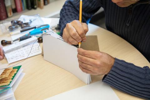 Shot of h和s using a pencil to bind several pages of a h和-made book together. 