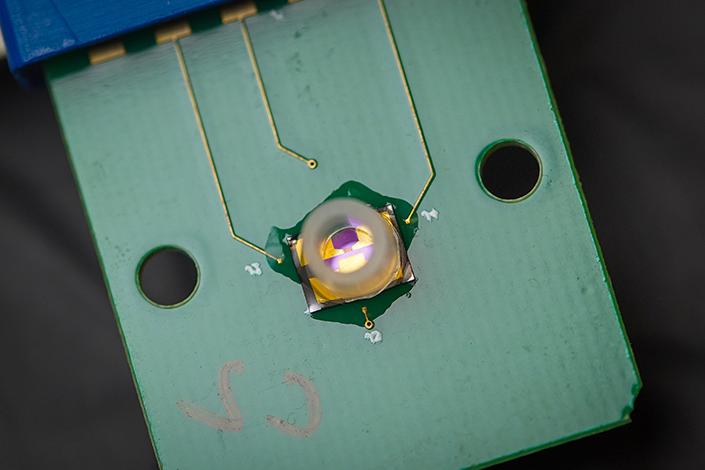 生物传感器的特写图像, 一个绿色的板条，在左边和侧面有一个洞, 表面连着三根电线, 通向一个带塑料环的中心枢纽