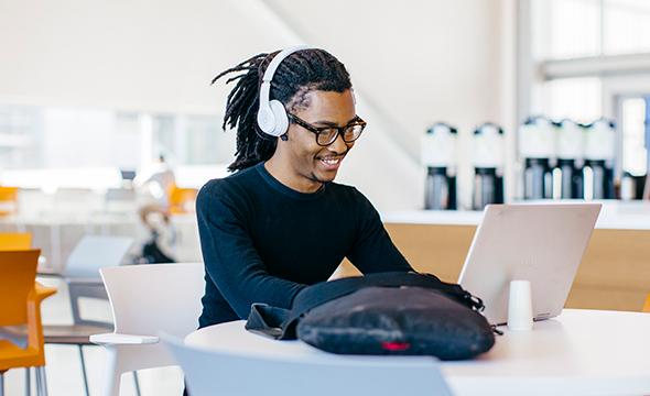 Young African American man smiling with headphones on working on a computer