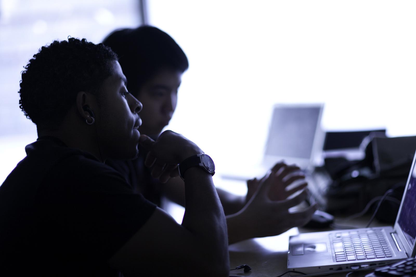 两个男大学生在笔记本电脑上打字. 他们的个人资料是可见的，但他们大多是背光的.