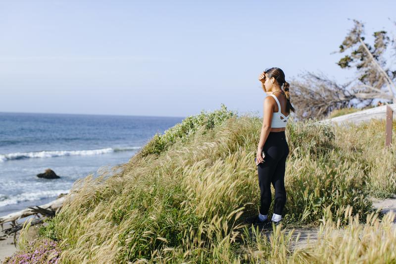 穿着运动服的年轻女子用手遮住眼睛，从长满草的悬崖上眺望大海.