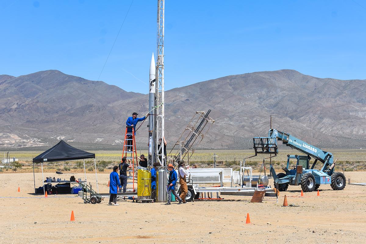 学生们在沙漠地面上准备发射火箭，背景是干燥的山脉