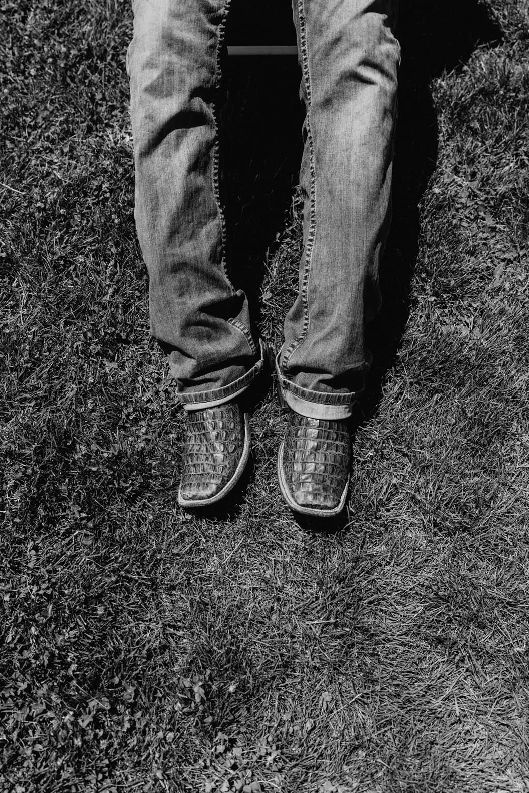 Black and white image of legs wearing jeans and cowboy boots against grass/dirt