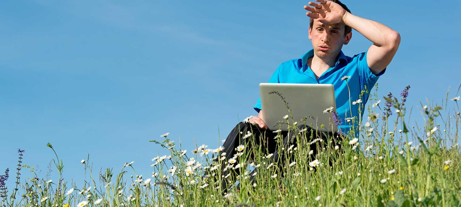 外面有个男人，坐在田野里拿着笔记本电脑，擦着额头上的汗