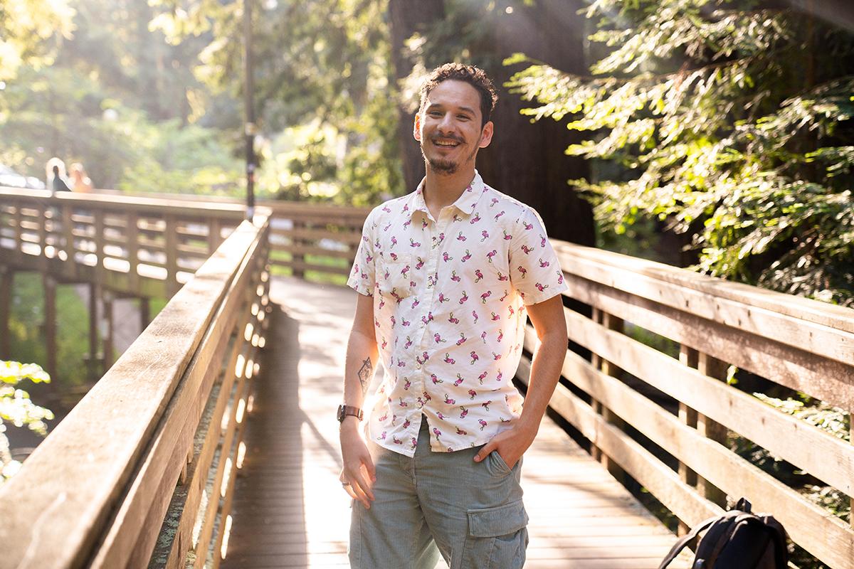 一个微笑的年轻人站在红杉树环绕的桥上