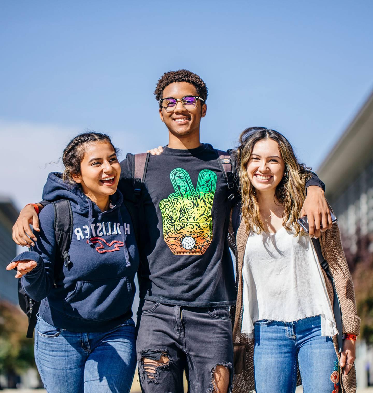 Three students with their arms around each other walking on campus