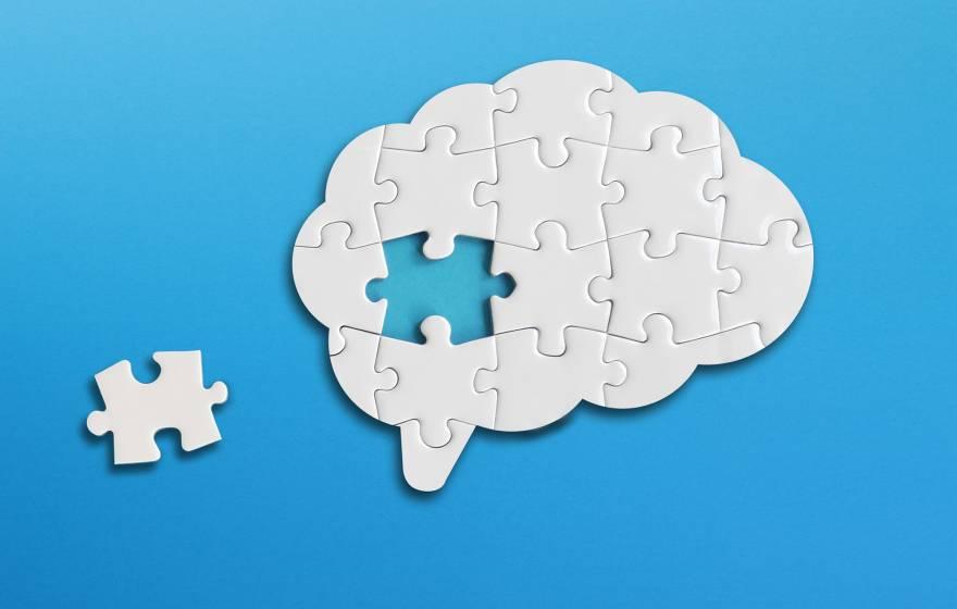 A puzzle of a brain with one piece to the side; puzzle is white on a blue background