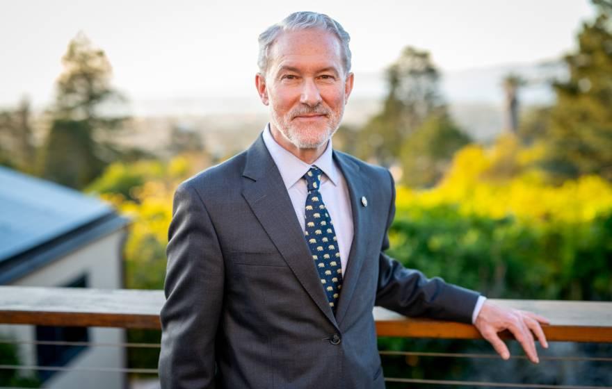 Rich Lyons, a white man with white hair and a white beard, smiling in a suit with a Berkeley bears tie, on campus