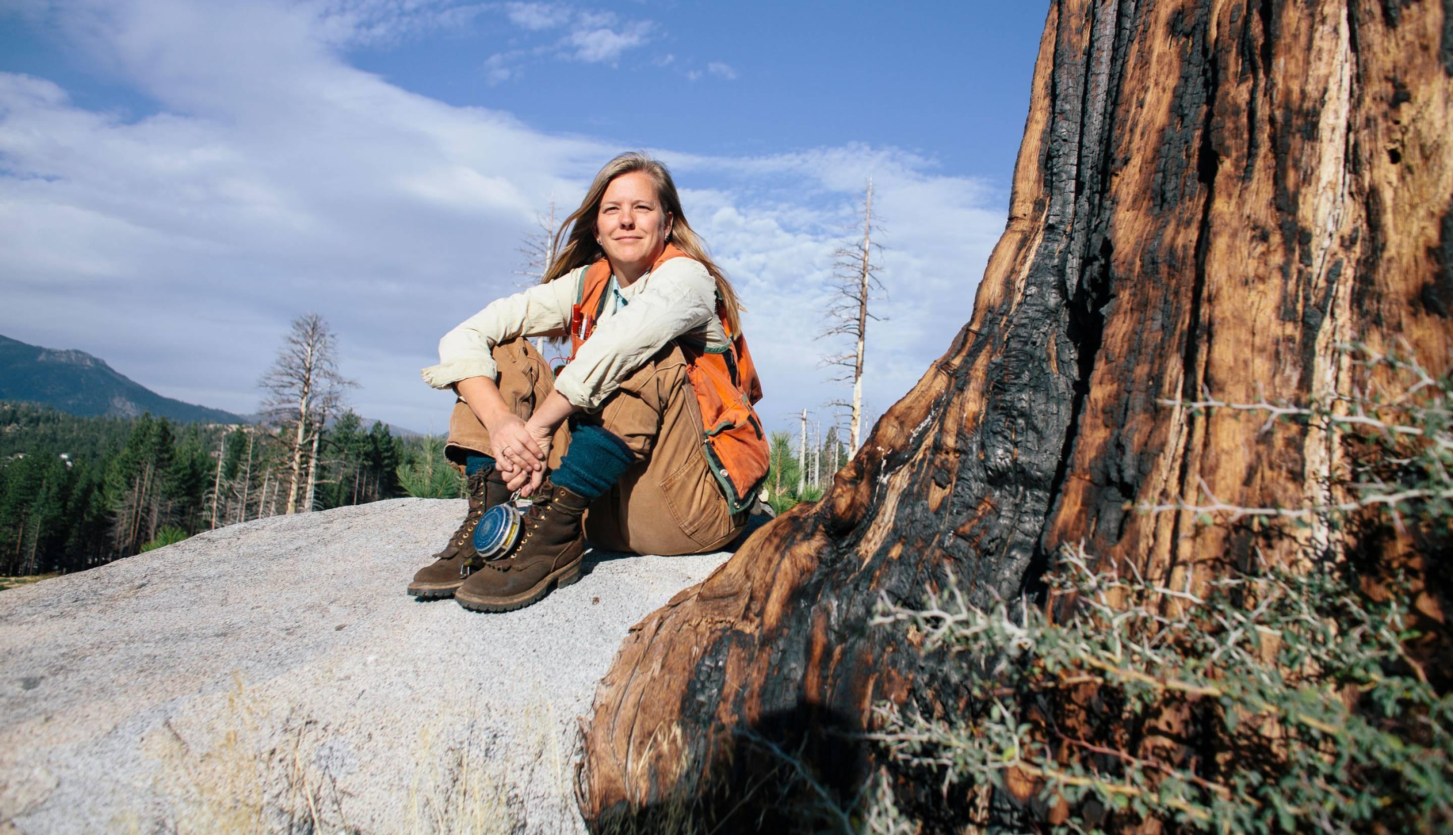 Woman sitting on a rock next to a large tree with burn marks