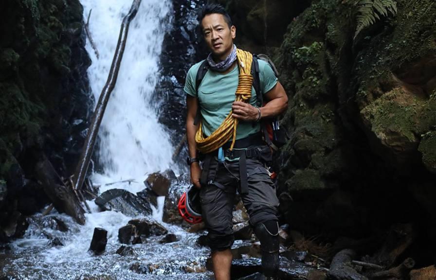 国家地理探险家带着攀岩装备站在瀑布前
