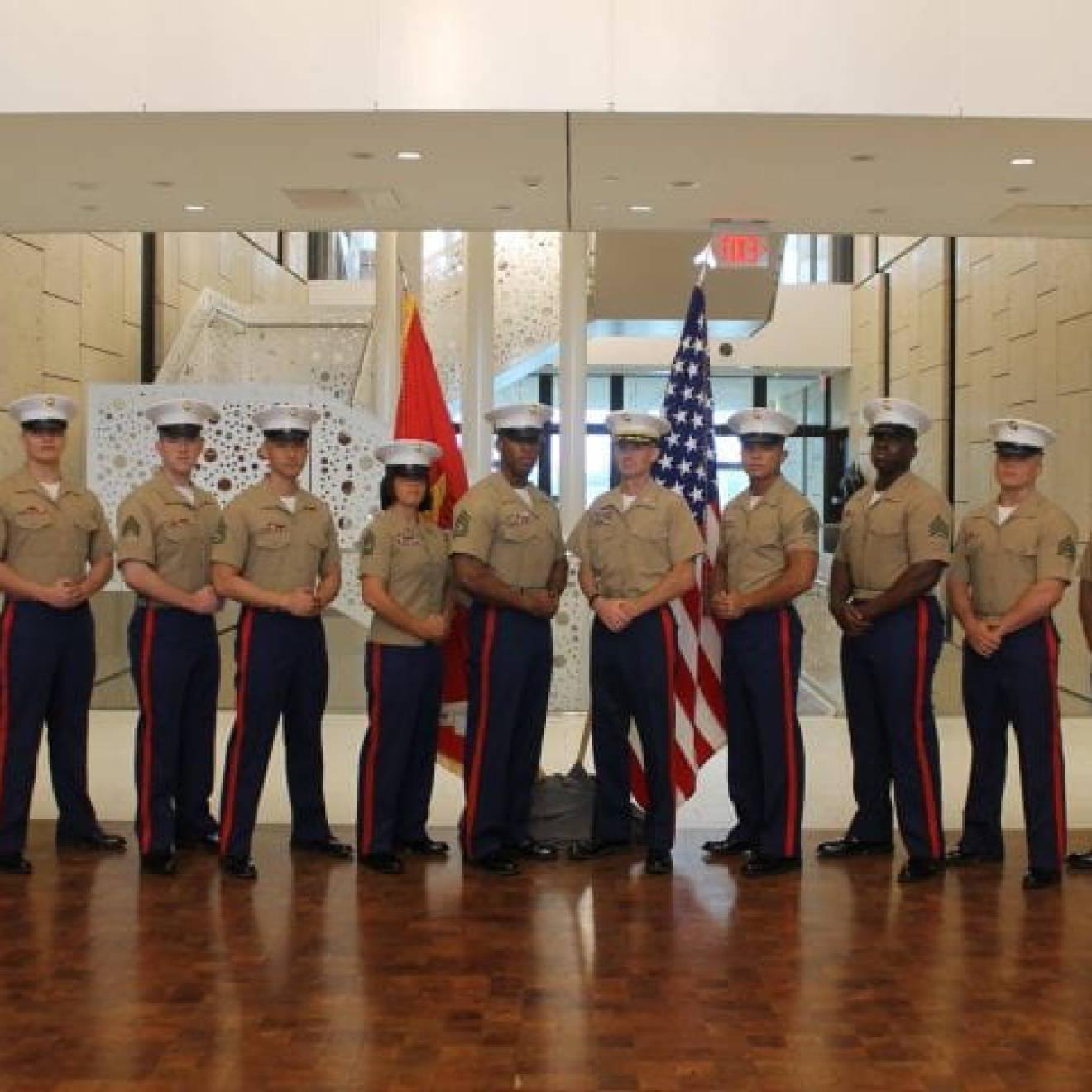 美国海军陆战队老兵，UCI社会学校友Andrew Truong ' 23(右四), pictured with fellow service members, posing at ease in their uniforms in front of flags.