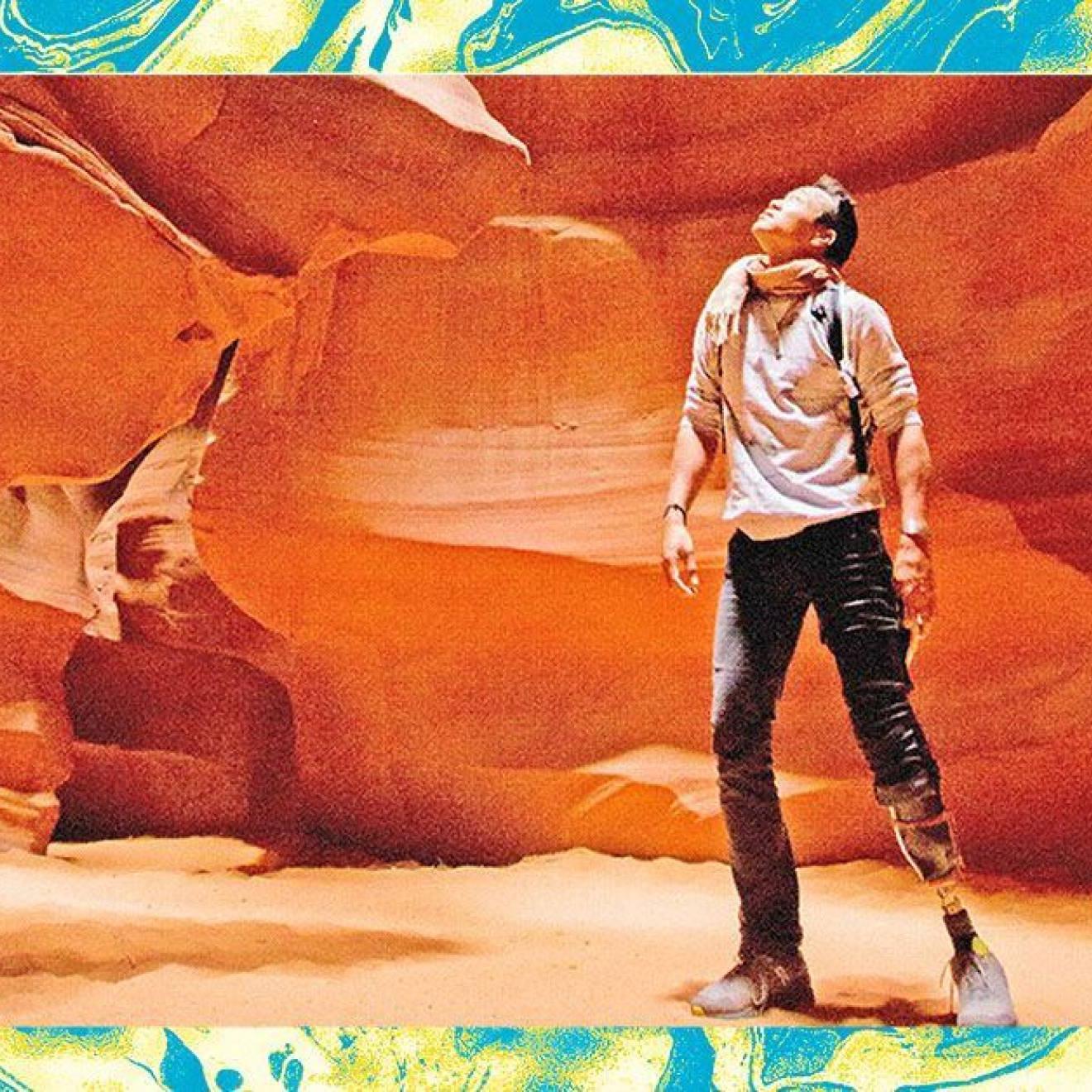 一位膝盖以下装着义肢的男性徒步旅行者仰望着峡谷的红色岩壁. 照片经过编辑和过滤，看起来颗粒状，周围是一个蓝绿色的纹理框架.