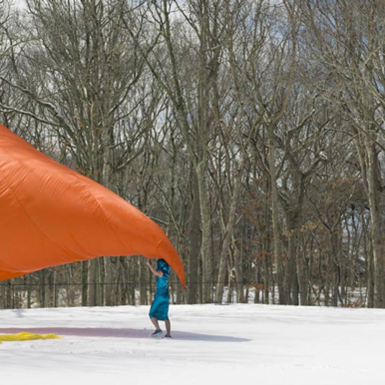 三个人在外面的雪地里用一块巨大的橙色床单表演
