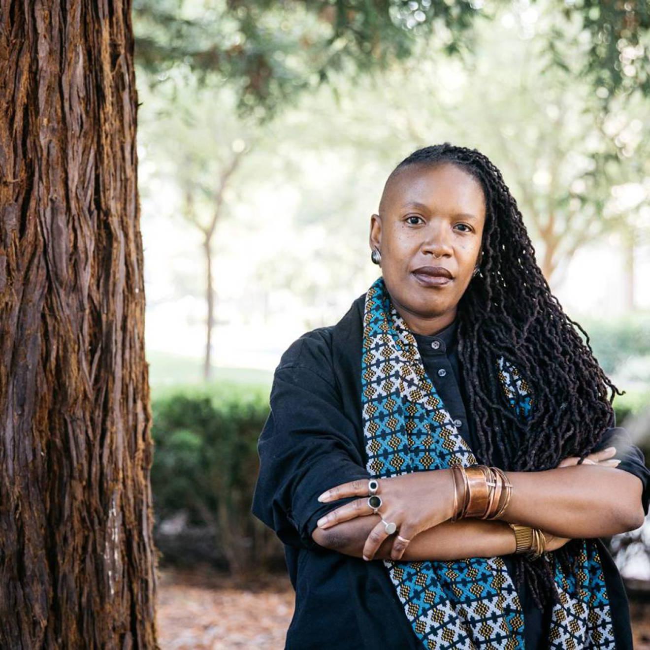 E. 非裔美国妇女Tendayi Achiume双臂交叉，在一棵红杉旁摆姿势